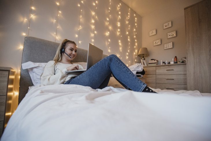 Student Using Laptop in Bed Surrounded by Fairy Lights