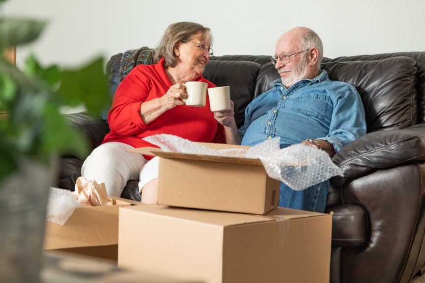 old couple surrounded by boxes having a cup of tea