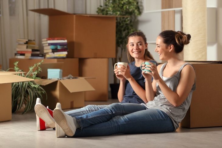 Students sat on the floor with a cup of tea smiling surrounded by boxes