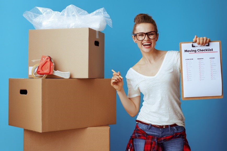 Woman smiling stood next to boxes and holding a packing checklist